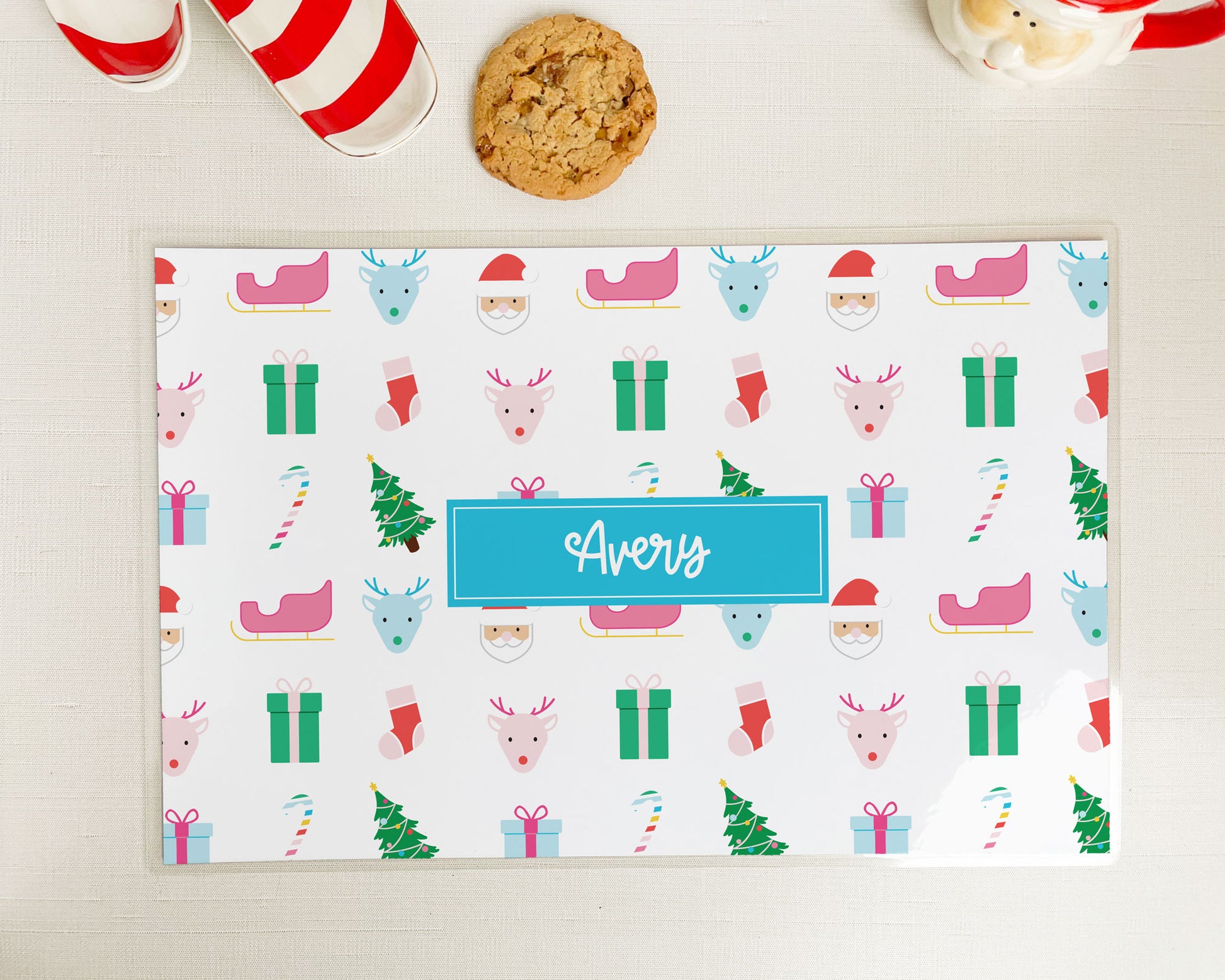 santa claus inspired christmas pattern, personalized laminated placemat, christmas decor, meredith collie paper, pink sleigh, green present, blue package, rainbow candy cane, blue pink reindeer, santa, red stocking
